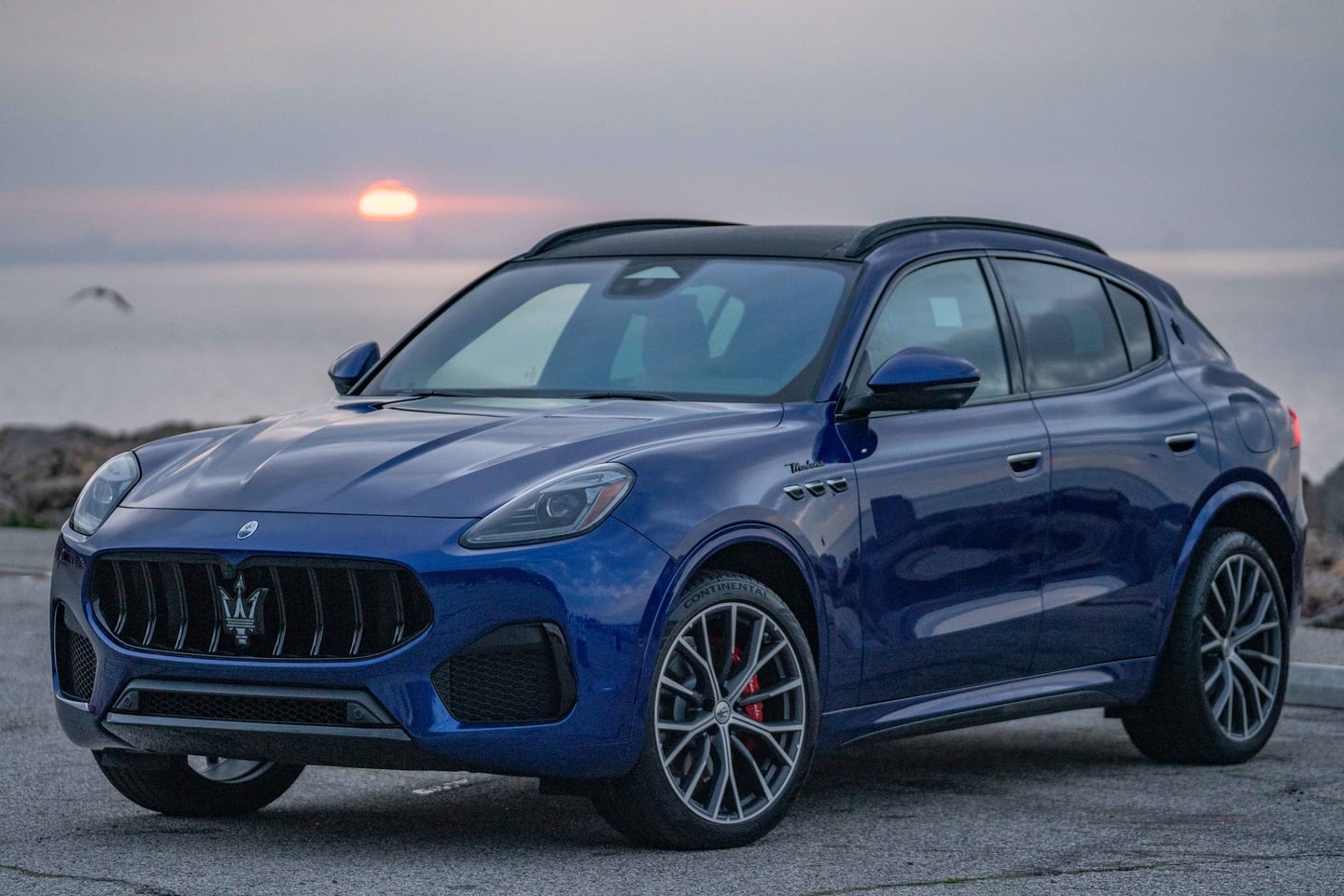 A blue Maserati Grecale Modena parked by the ocean at sunset at a goop Maserati event