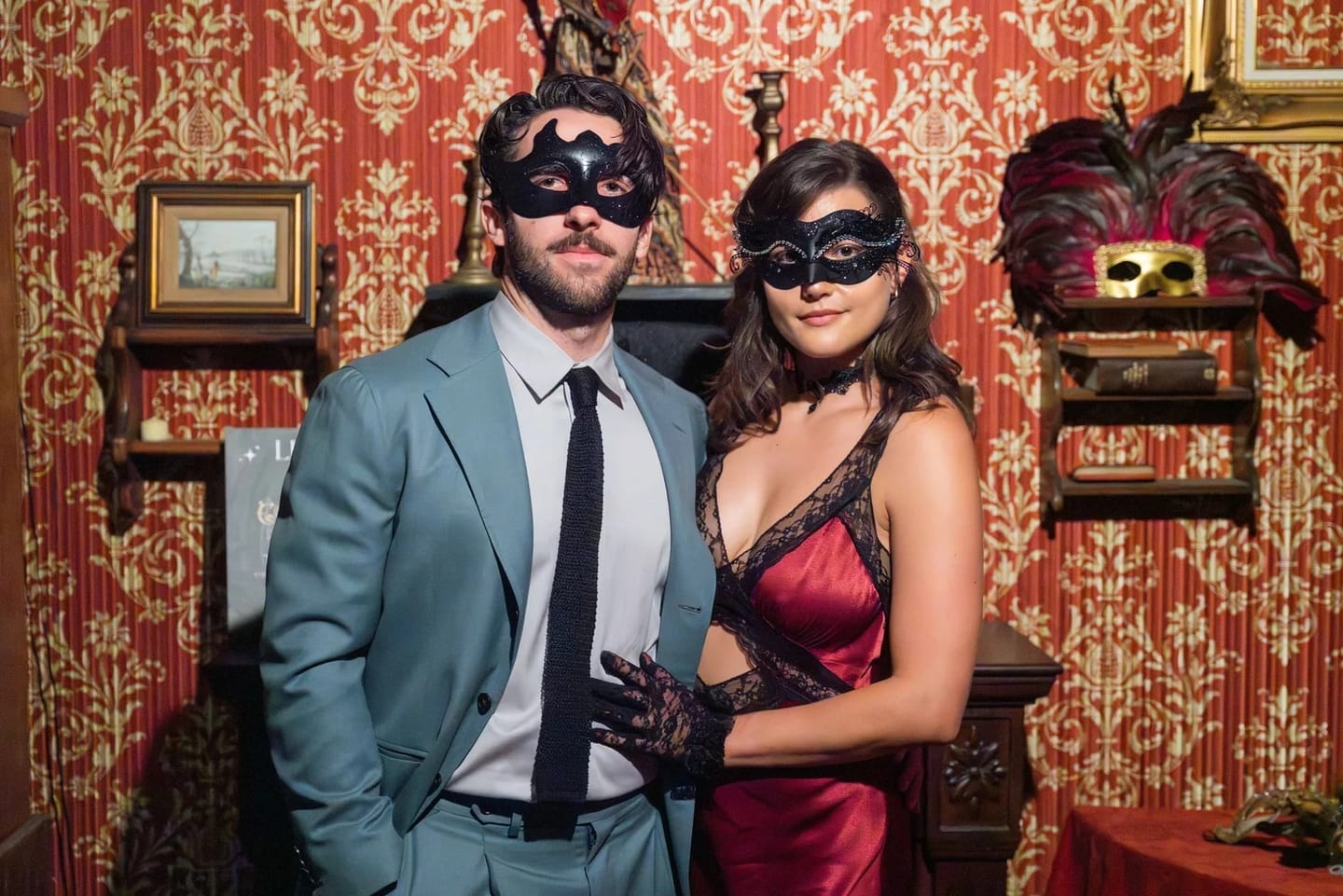 A couple in masquerade masks and formalwear at a private masquerade reception in a richly decorated Los Angeles room