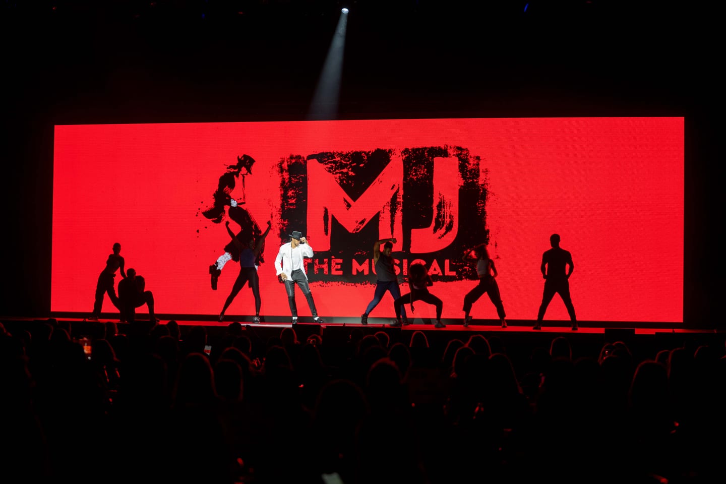 Dancers from MJ the Musical silhouetted against a giant red MJ logo screen while performing on stage at an IPW Broadway showcase