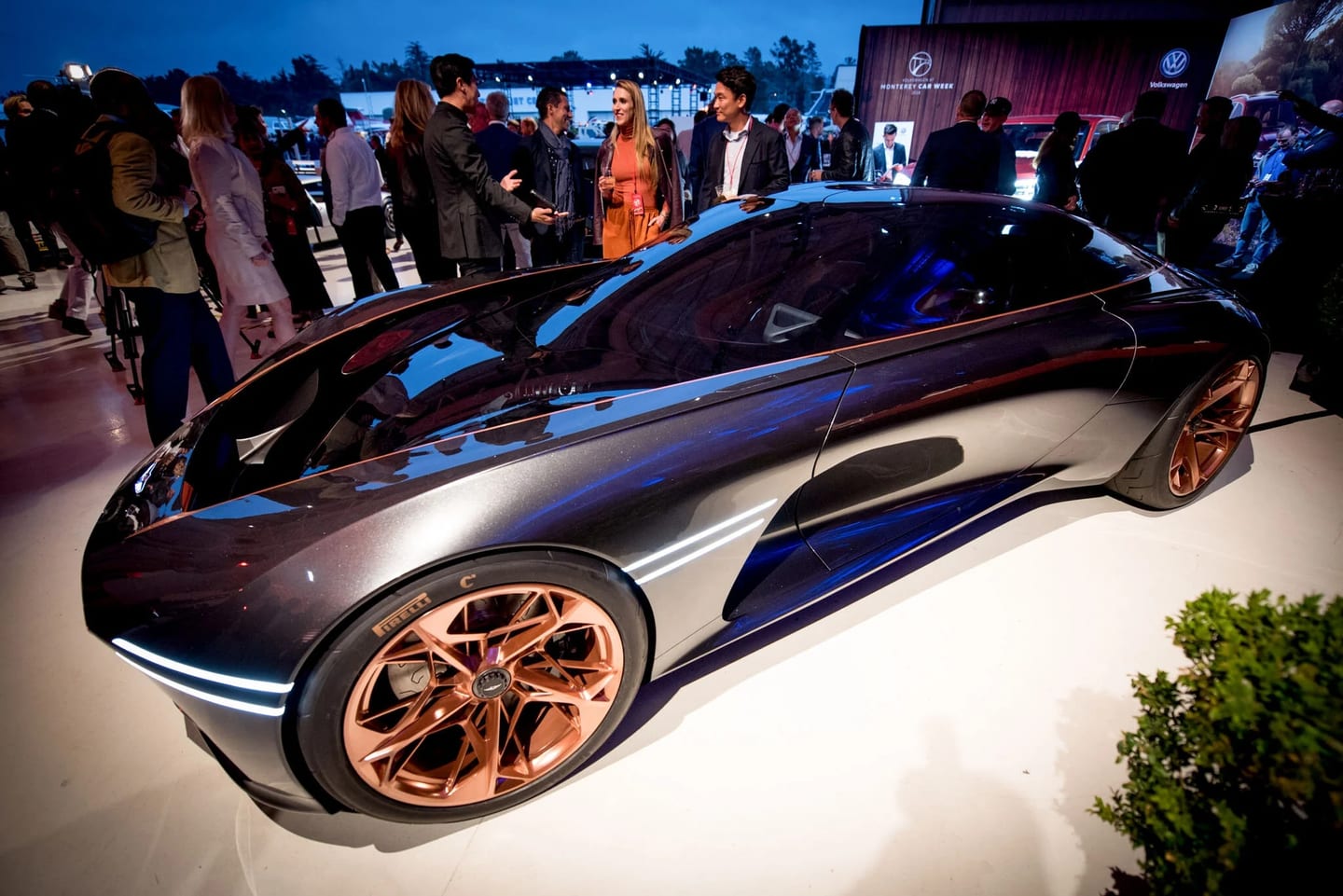 A dark concept car with copper wheels surrounded by guests at a Monterey Car Week event