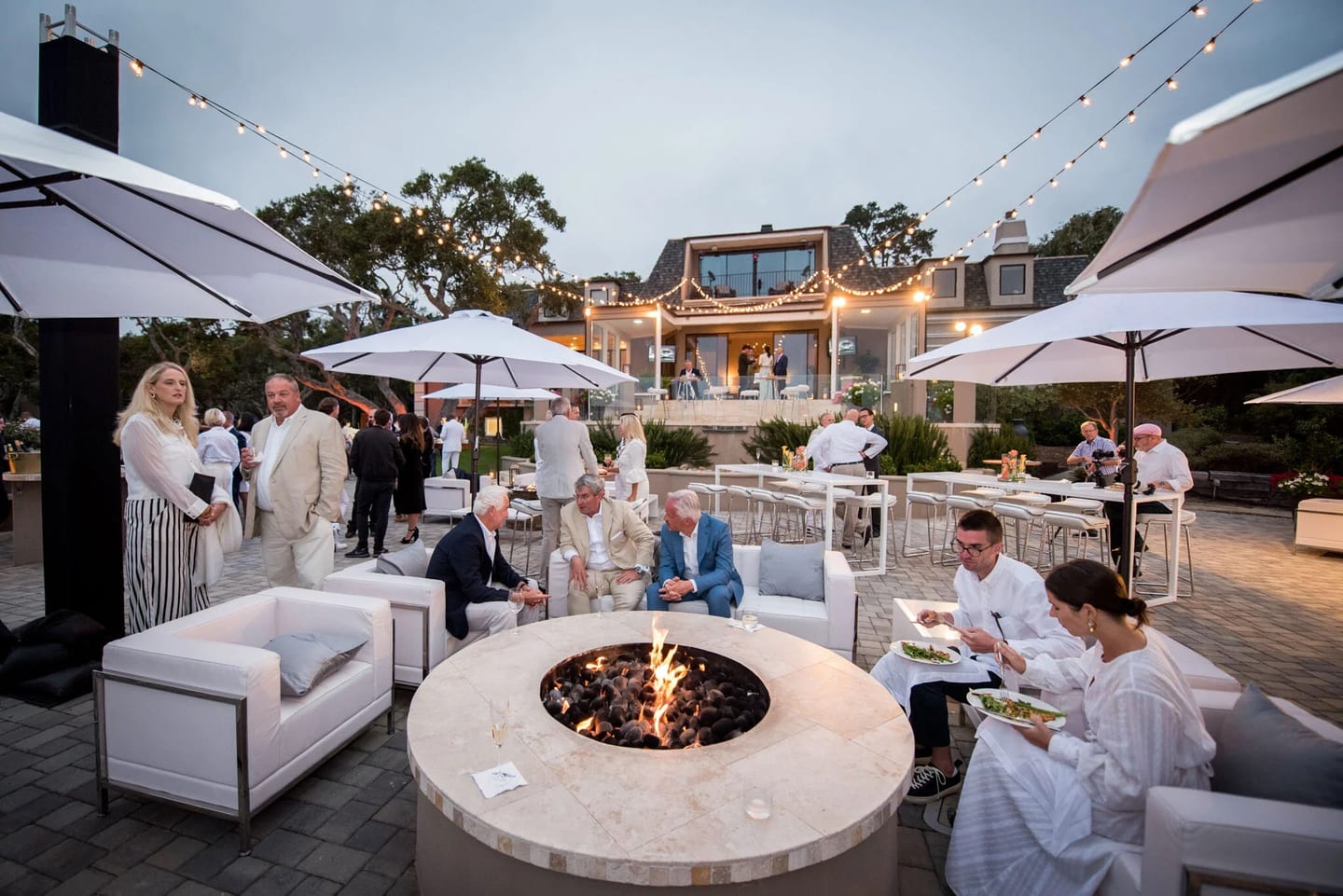 Guests gathered around a fire pit beneath string lights at a private Monterey Car Week estate party