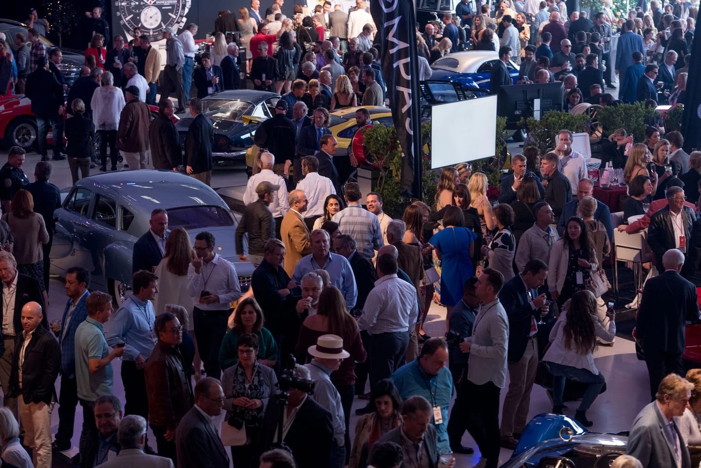 A crowded Monterey Car Week show floor filled with guests and classic automobiles