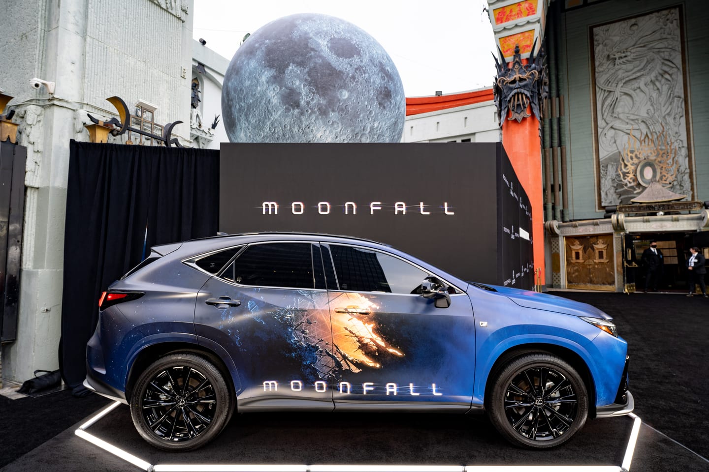 A Lexus NX wrapped in Moonfall film graphics on a lit display platform beneath a giant moon sphere and MOONFALL branding at the TCL Chinese Theatre in Hollywood