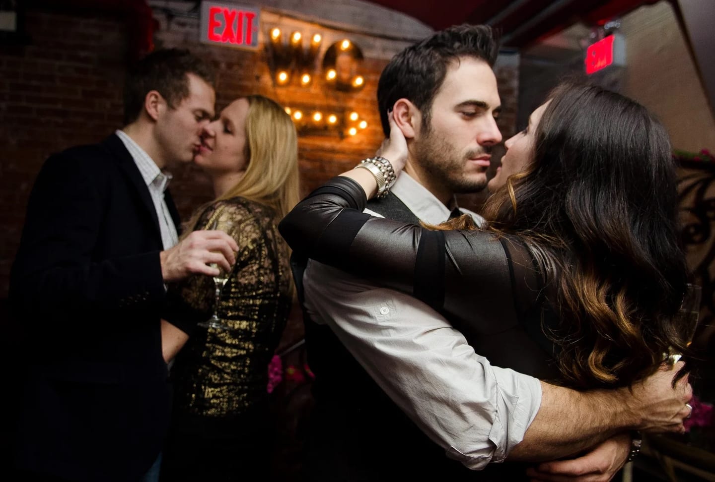Two couples kissing at midnight under marquee lights at a private New Year’s Eve party