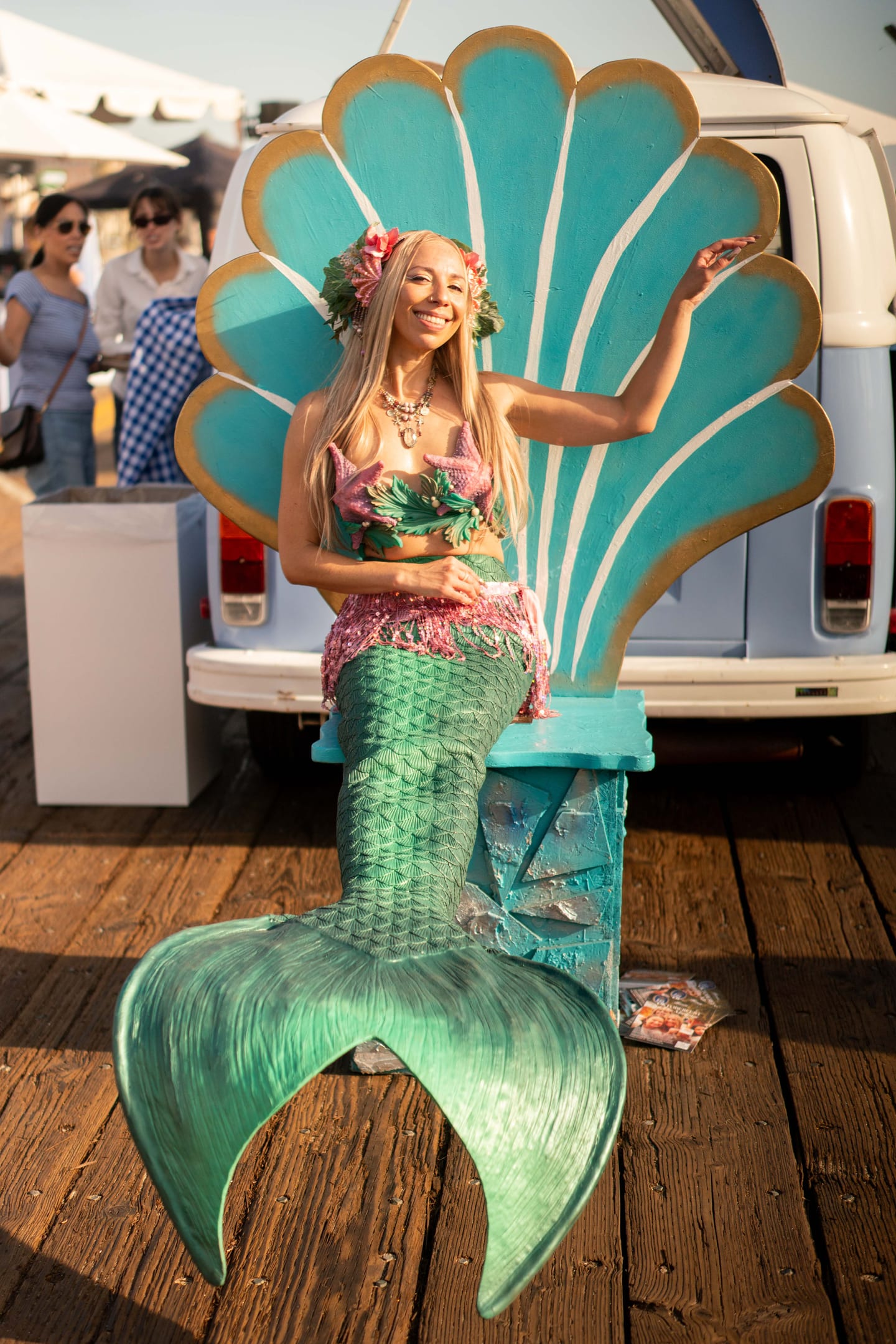 A mermaid performer in a green tail posing in a giant seashell throne on the Santa Monica Pier at the Off the Hook seafood festival