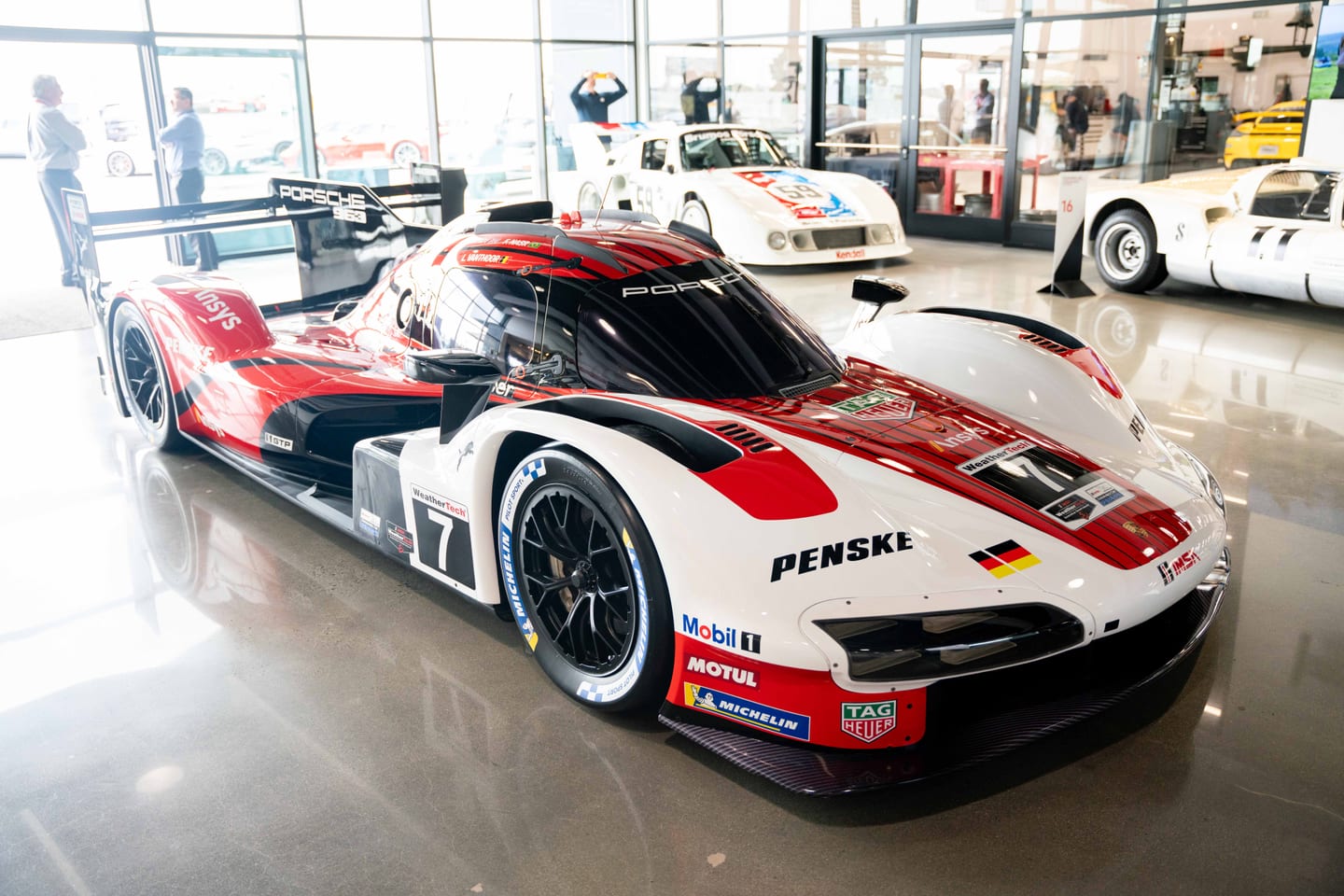 A red and white Porsche 963 Penske race car on display in the lobby of the Porsche Experience Center