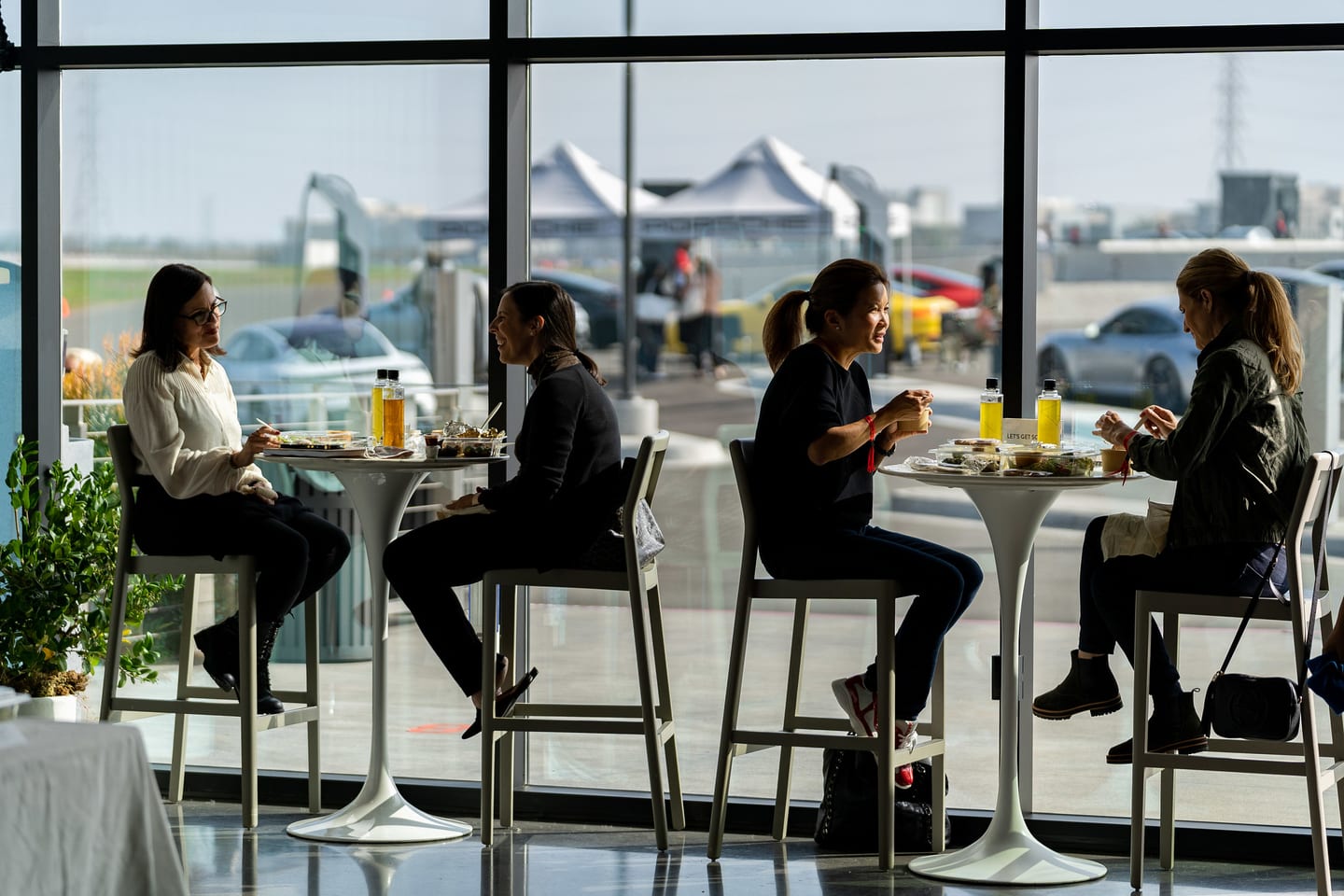 Guests at high-top tables by floor-to-ceiling windows overlooking the track and Porsche tents at the Porsche Experience Center Los Angeles