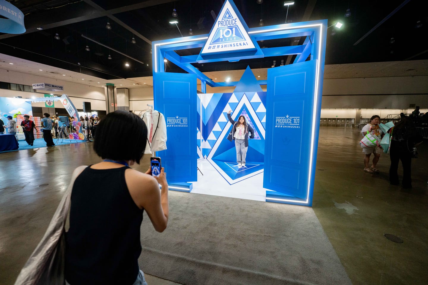 A visitor photographing a friend inside the blue Produce 101 The Shinsekai doorway activation at KCON LA 2025