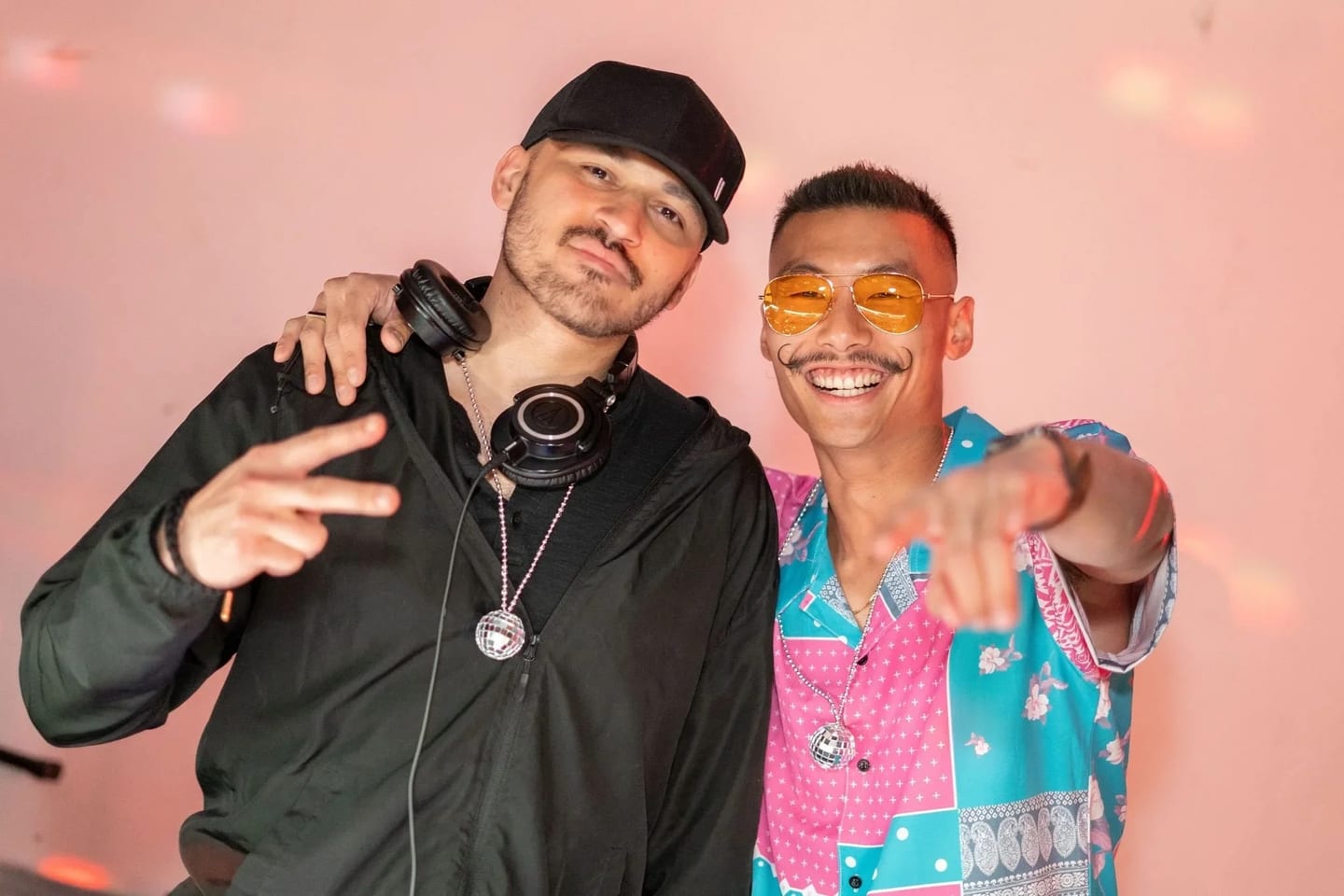 Two DJs posing together under pink light at a record release party