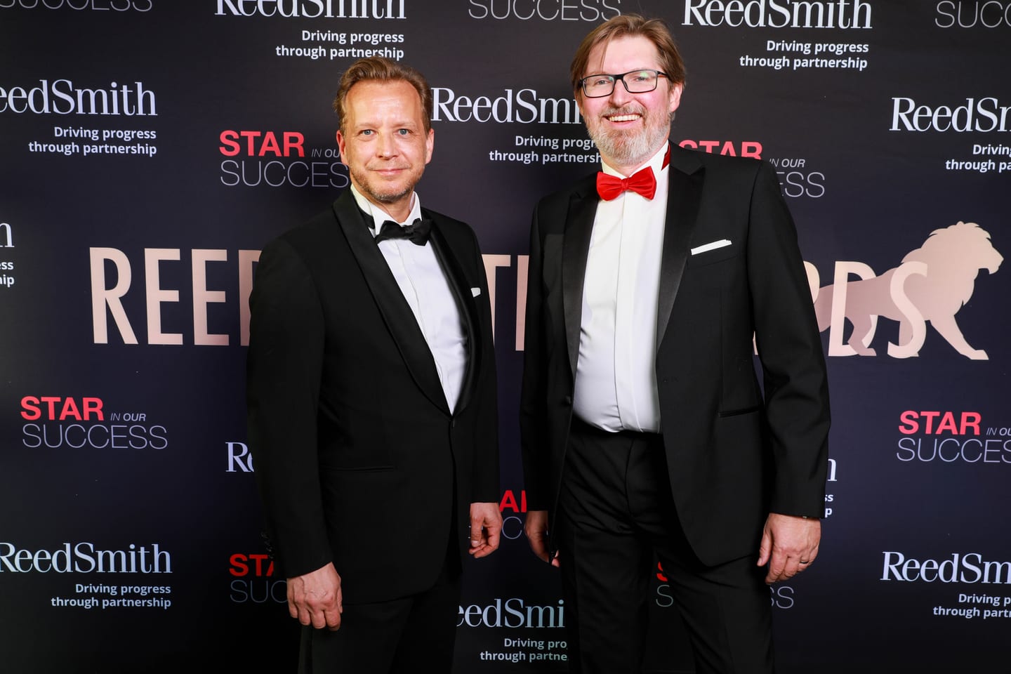 Two men in black tie on the Reed Smith “Star Success” step-and-repeat at an awards gala