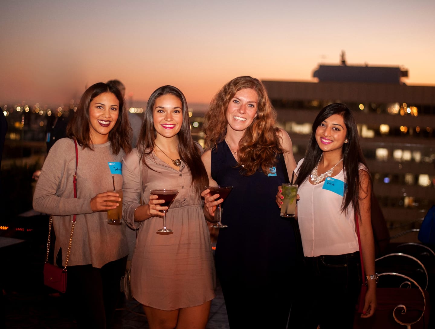 Four guests holding cocktails on a rooftop at sunset