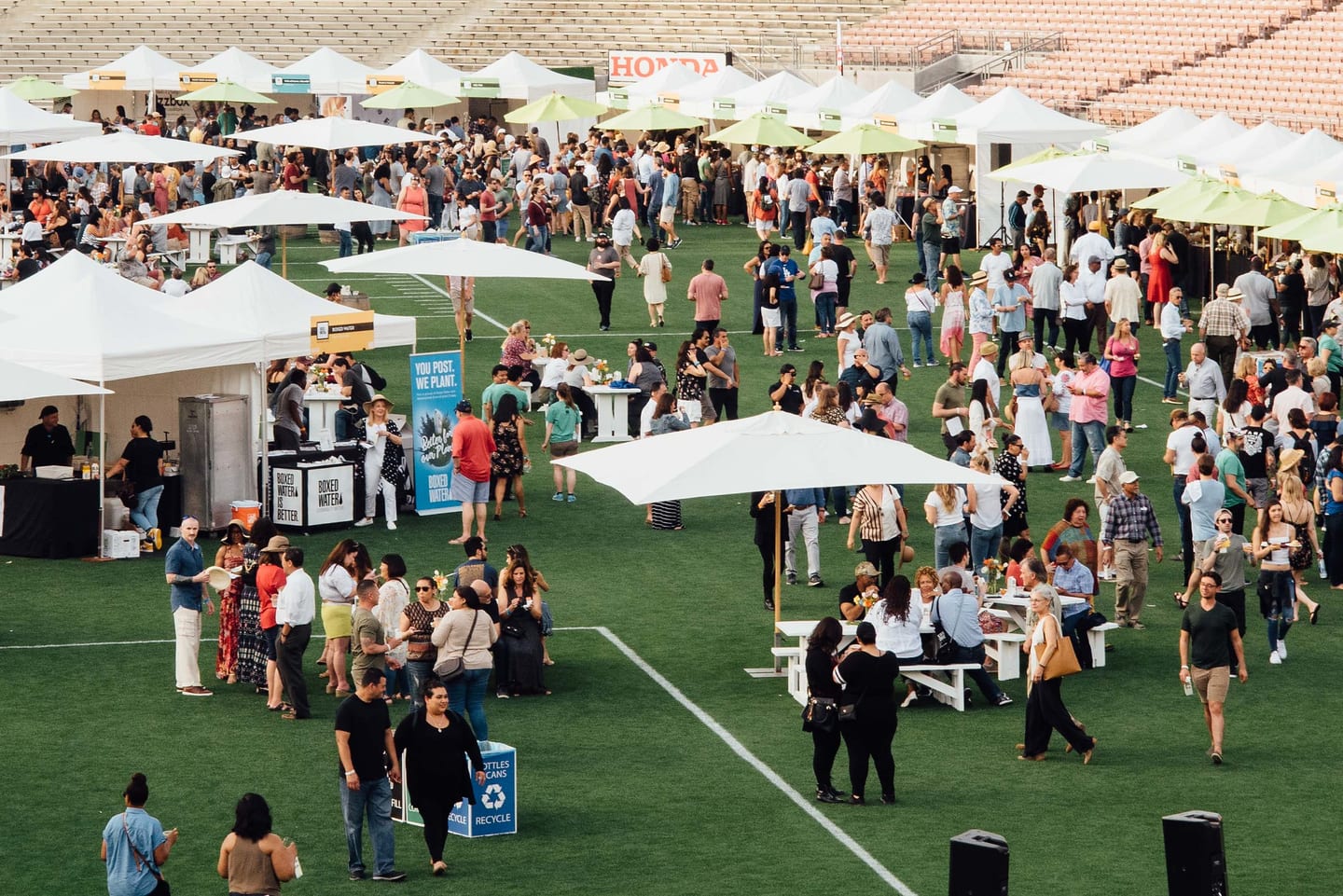 An elevated view of a dense festival crowd among white vendor tents and umbrellas on the Rose Bowl field in Pasadena