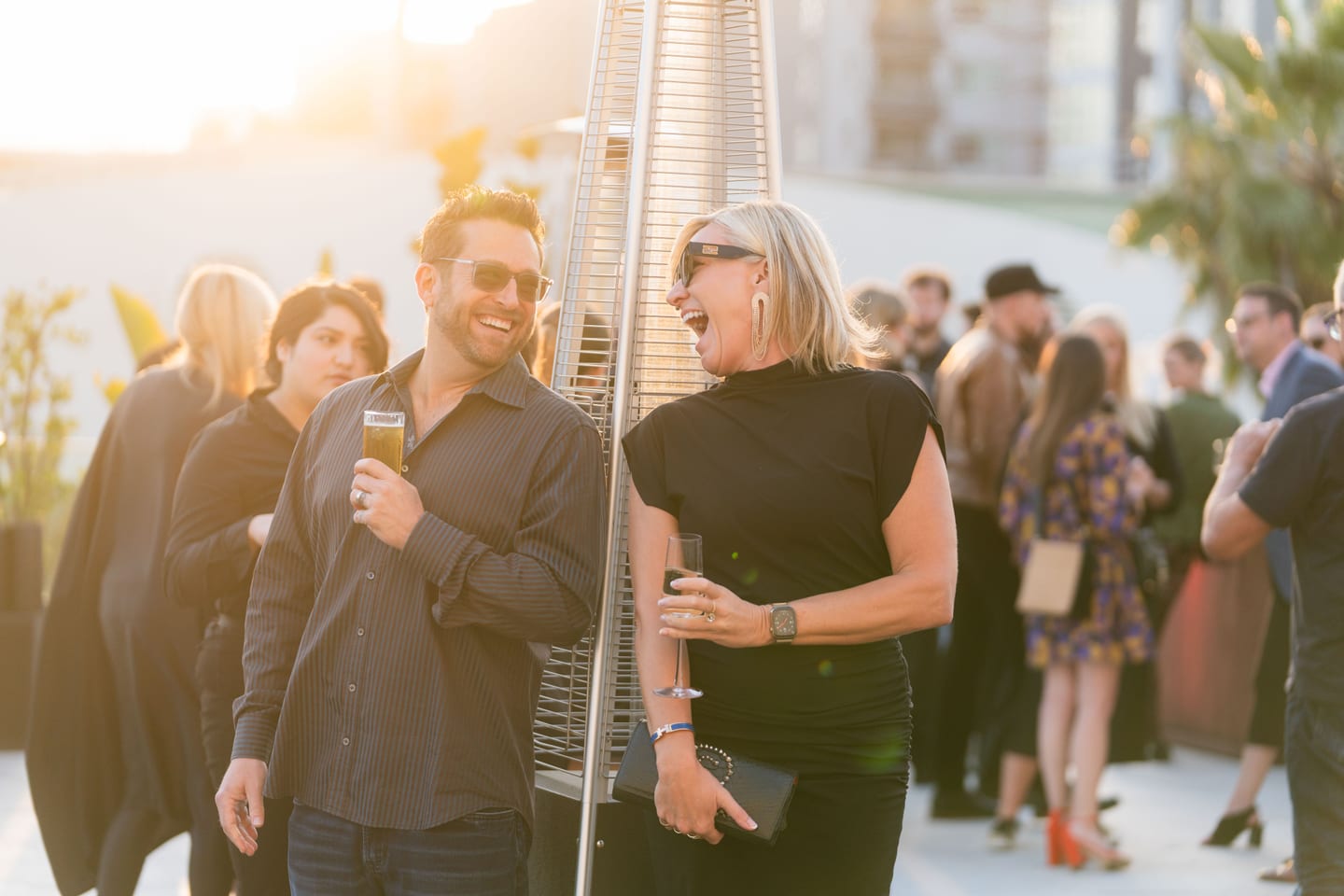 Two guests laughing together at golden hour on a rooftop at a Los Angeles event