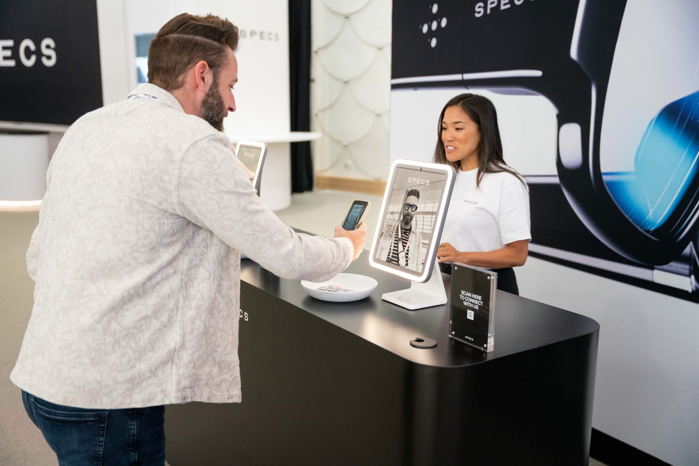A Snap staff member showing a demo on a tablet to an attendee across a black SPECS counter
