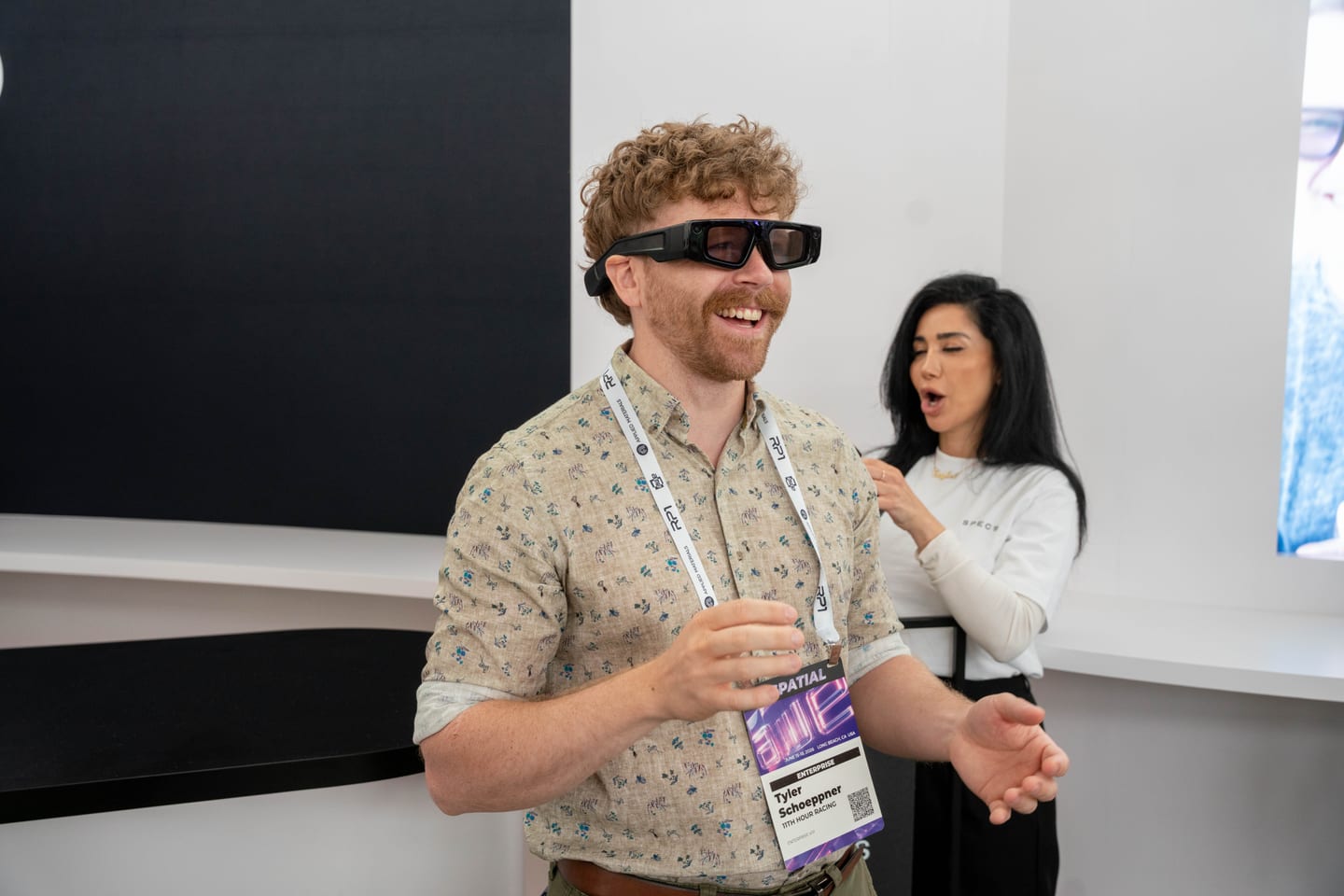 A smiling attendee wearing Snap Specs reacting mid-demo while a staff member watches from behind