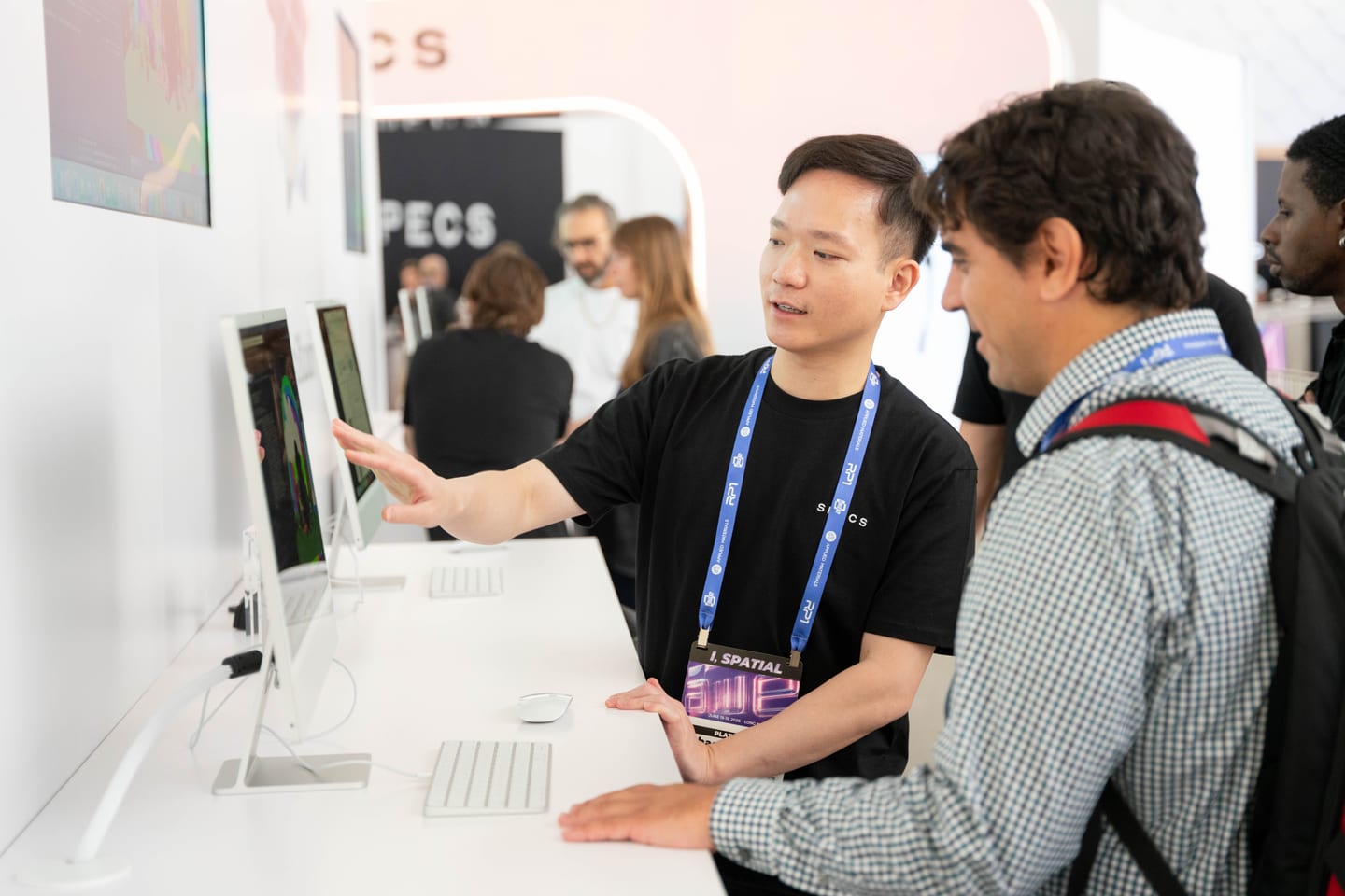 A Snap team member pointing at a monitor while showing Lens Studio to an attendee at the SPECS demo bench