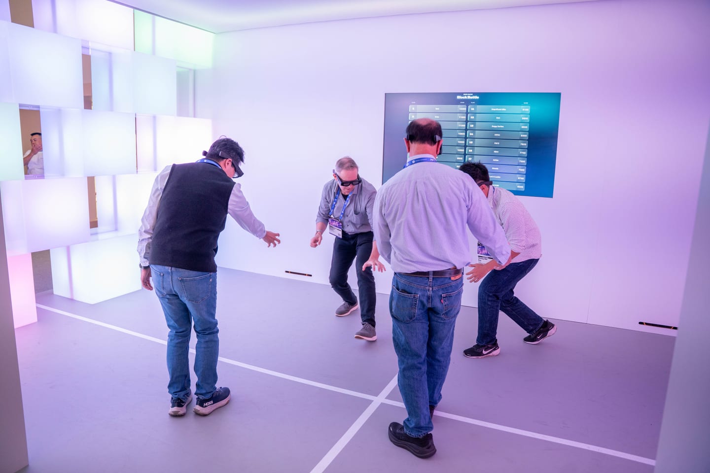Four men wearing Snap Spectacles crouching and reaching mid-game in a glowing demo room with a scoreboard on the wall