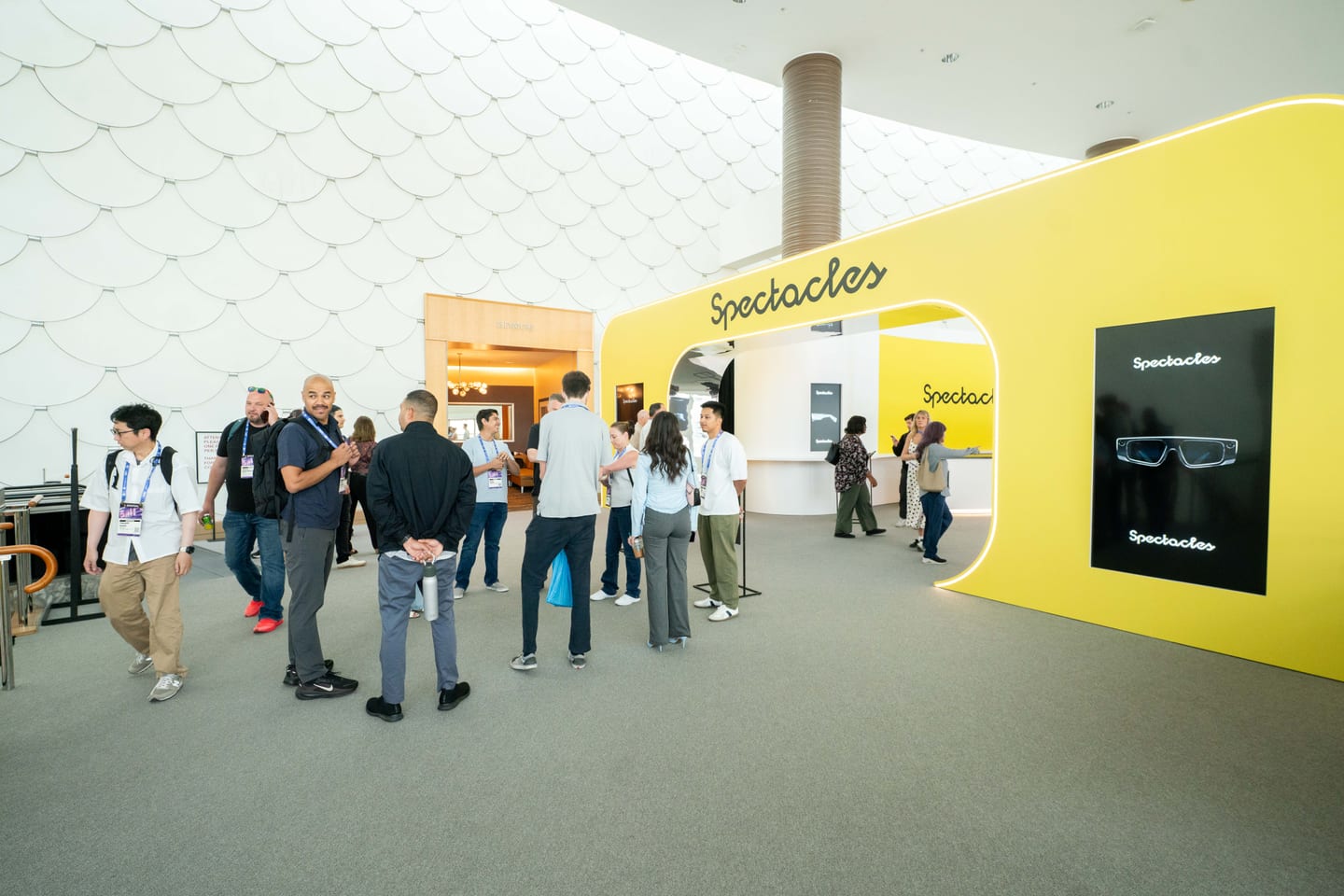 Attendees walking past Snap’s bright yellow Spectacles stand in the Long Beach Convention Center concourse
