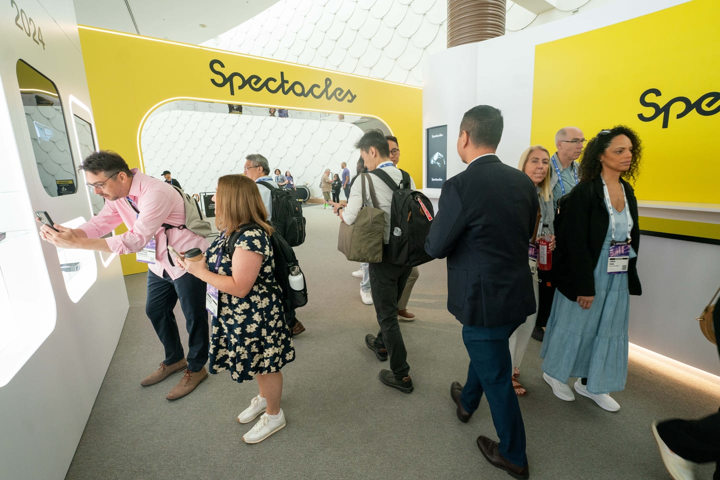 Attendees trying devices at demo stations along a bright yellow Spectacles corridor at Augmented World Expo