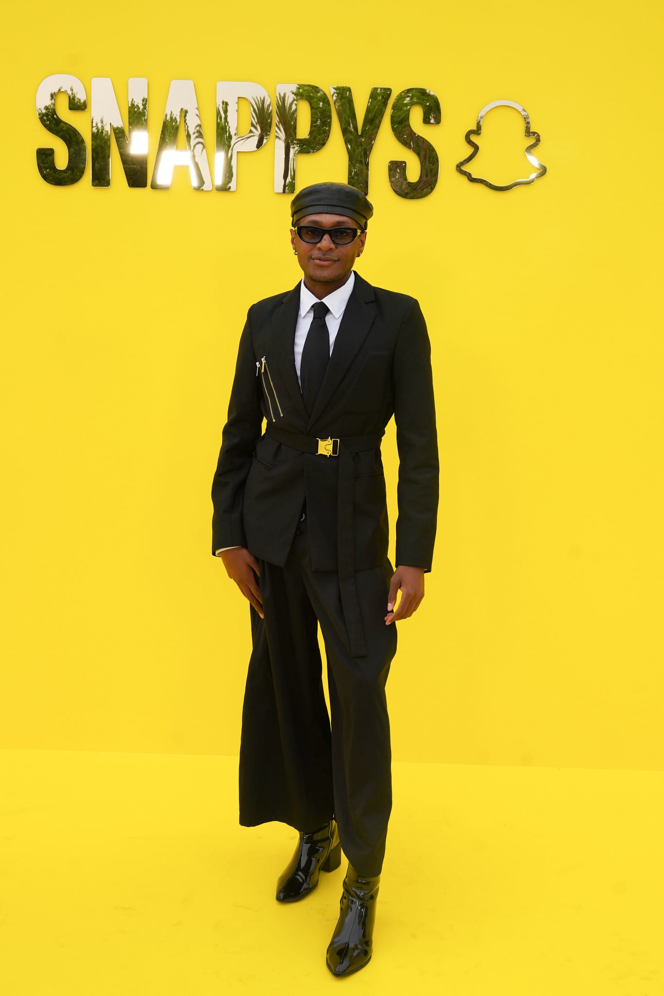 Creator Steven Clark in a belted black suit, leather beret, and patent boots on the yellow carpet at the SNAPPYS, Snapchat HQ