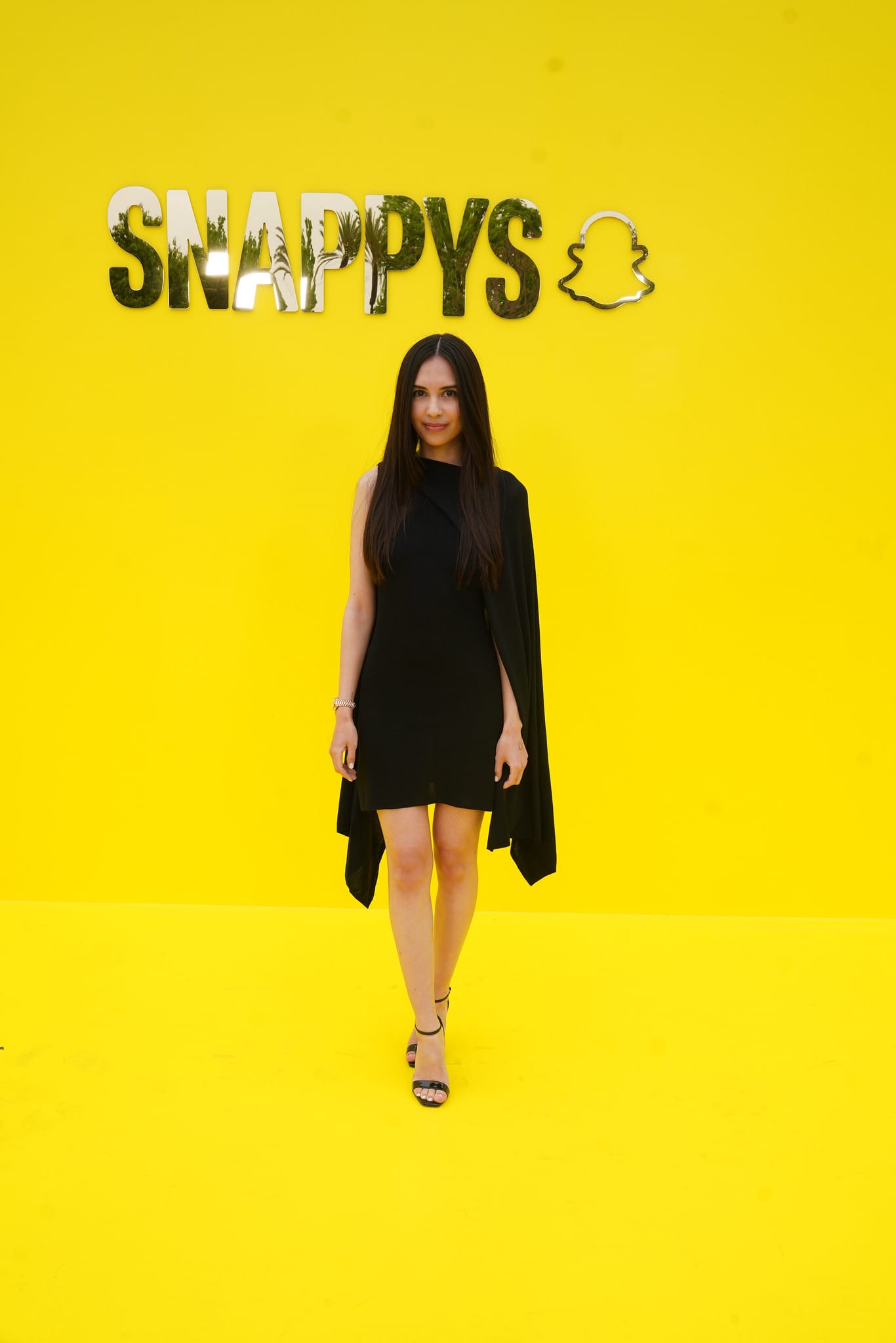 Guest in a black cape dress posing on the yellow carpet under the SNAPPYS sign at Snapchat HQ