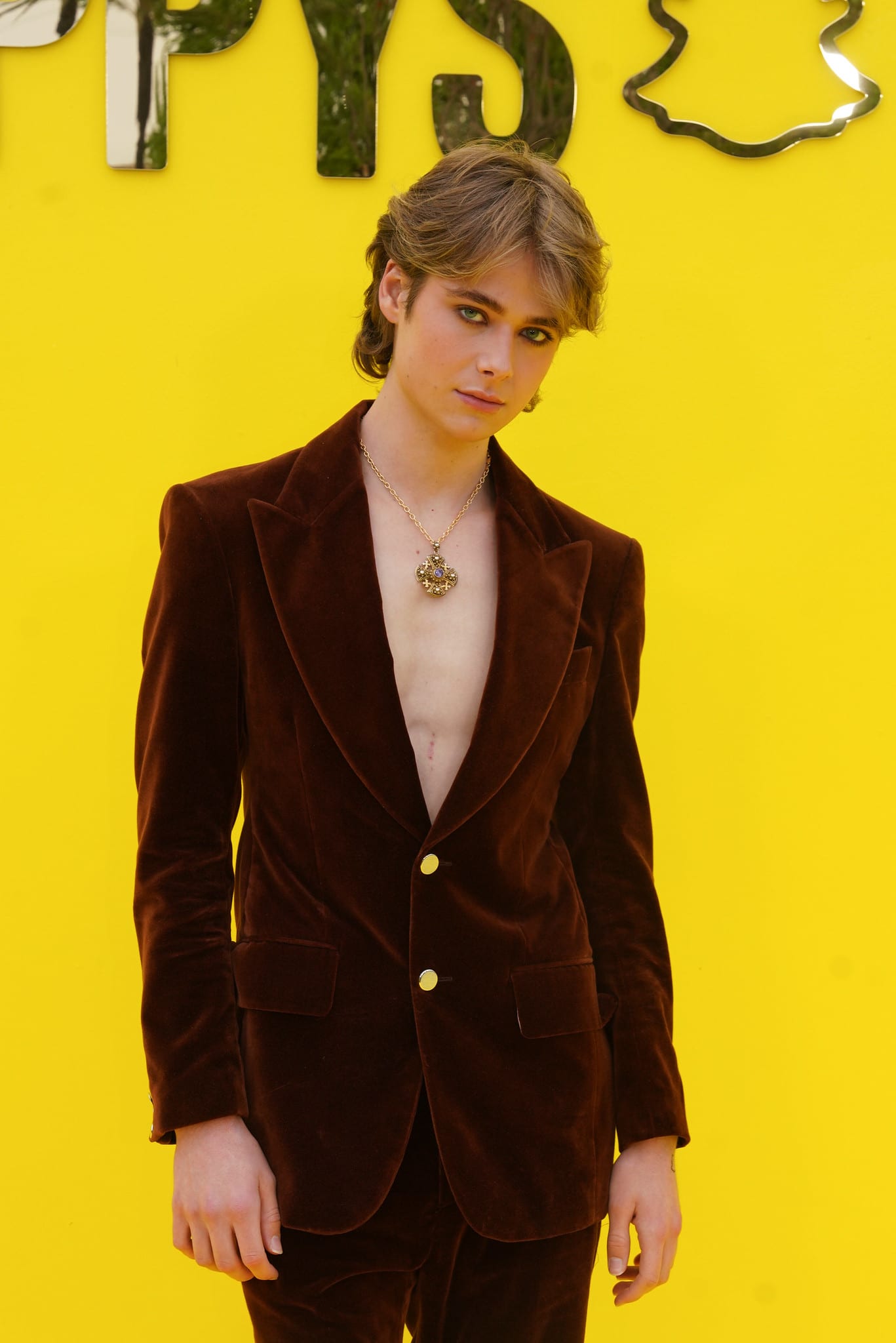 Creator in an oxblood velvet suit and gold pendant posing on the yellow carpet at the SNAPPYS, Snapchat HQ