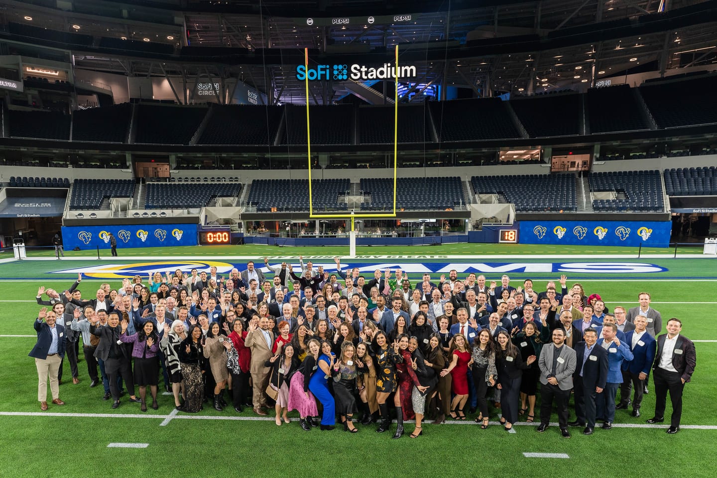 The team from Aristotle Capital Management, a Los Angeles investment firm, waving together on the field at SoFi Stadium with the stadium name and Rams branding behind them