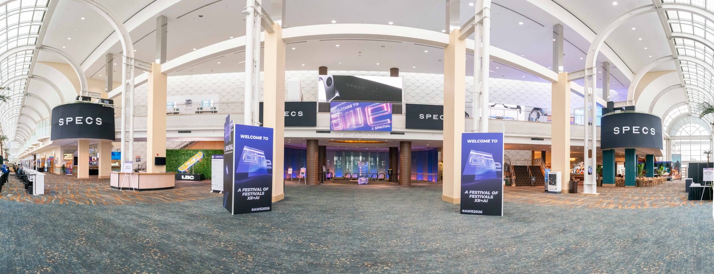 An ultra-wide view of the SPECS XR and AI festival entrance in a convention center concourse, with SPECS signage and lit welcome towers under a vaulted glass ceiling