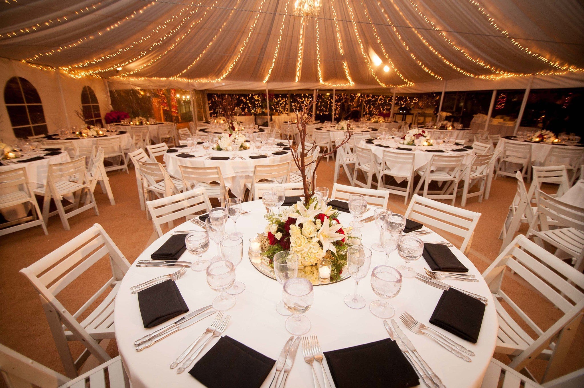 Elegant tented gala dinner with round tables and string lights at an event