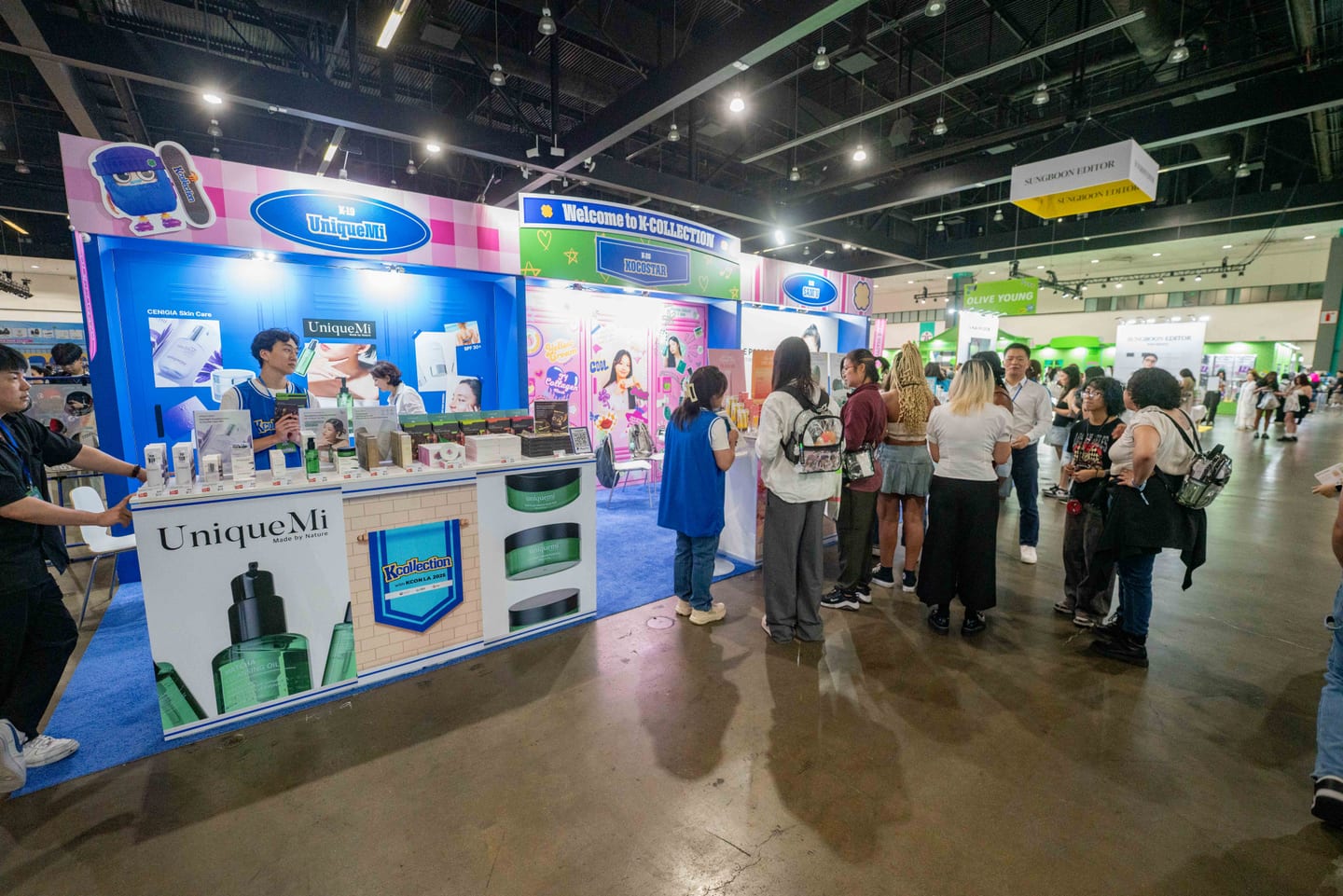 The UniqueMi skincare booth under a Welcome to K-Collection sign at KCON LA 2025, with attendees browsing product displays