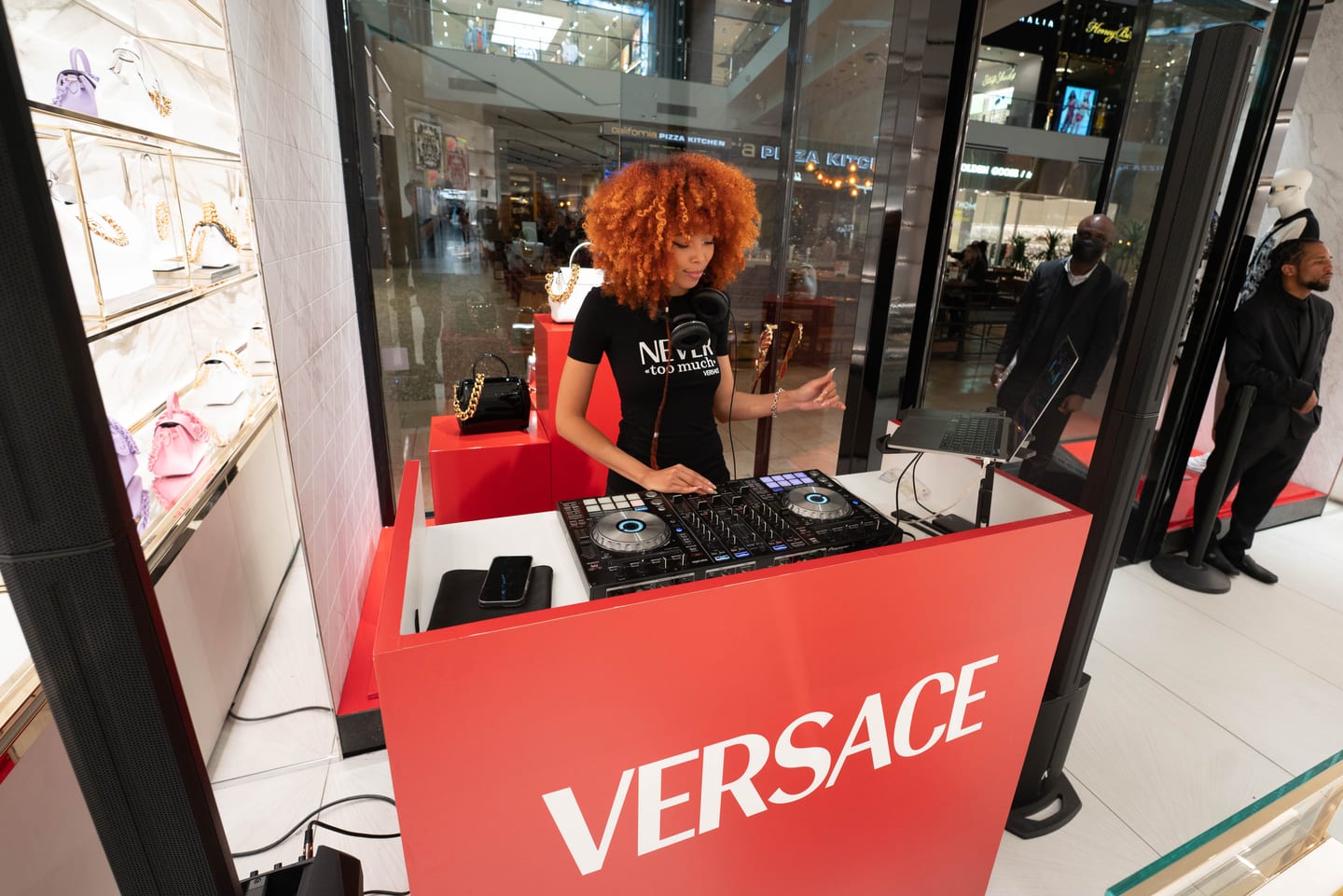 A DJ spinning behind a red Versace pop-up counter beside a handbag display at Westfield Topanga in Los Angeles