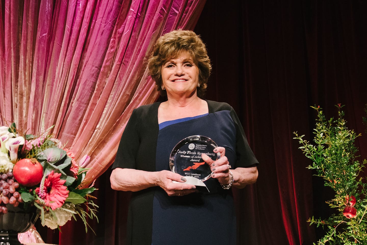 Honoree holding her award in front of pink drapes at the Women of Achievement luncheon