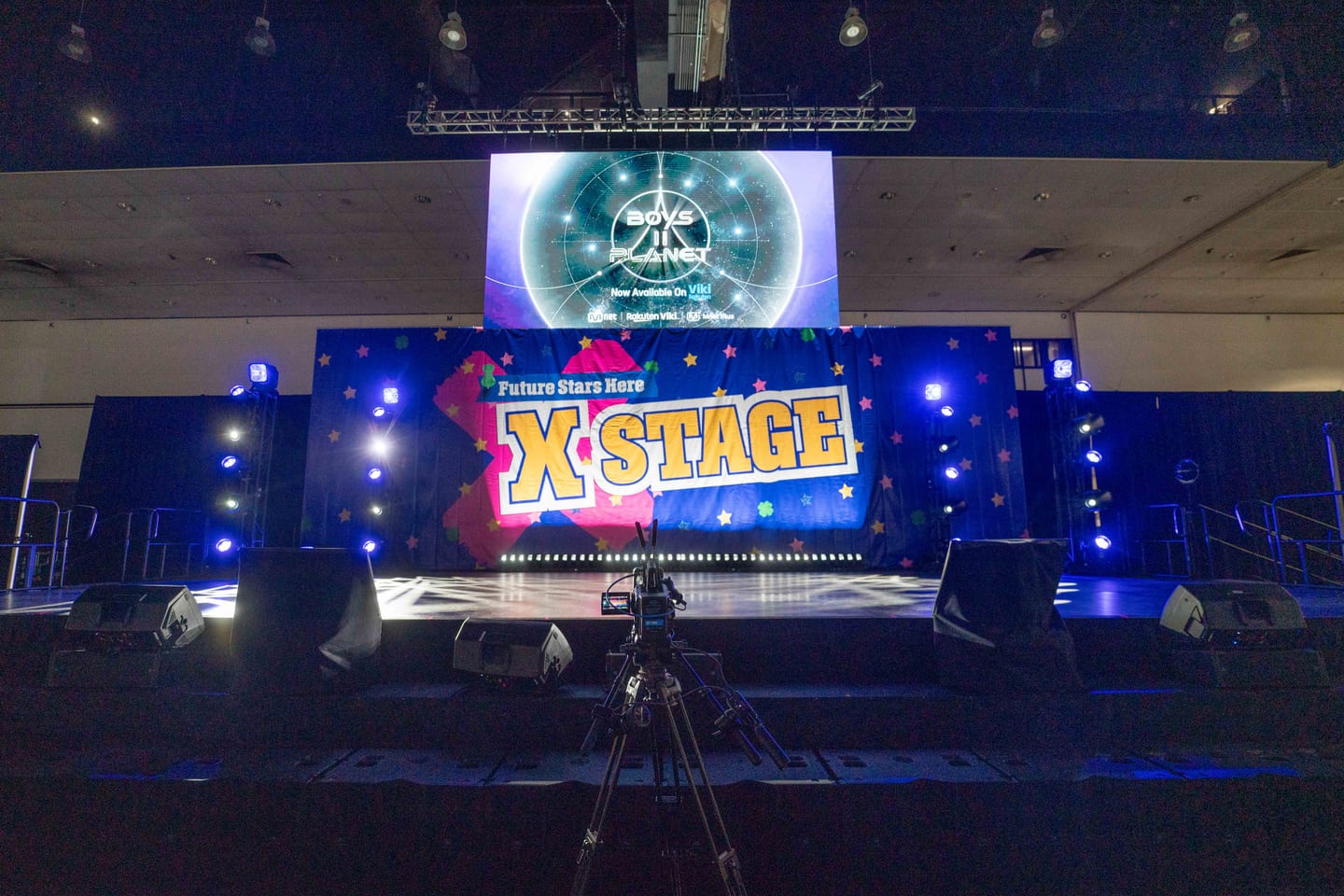 The empty Future Stars Here X Stage at KCON LA 2025 lit blue before doors, with a Boys II Planet screen above it