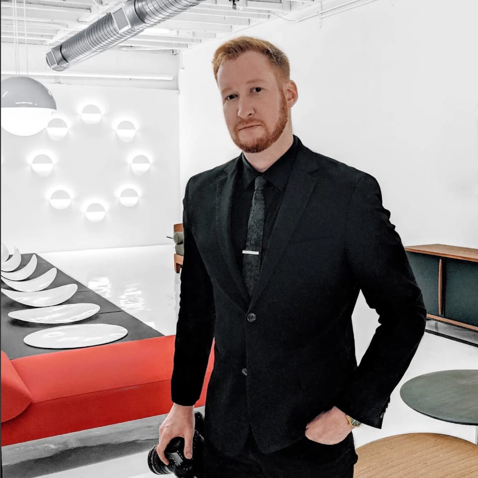 Andrew Heiser in a black suit holding a camera in a modern interior
