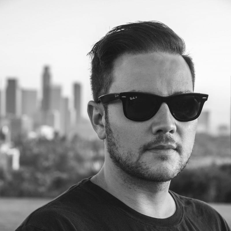Black-and-white portrait of Brandon Ogden wearing sunglasses with the Los Angeles skyline behind him
